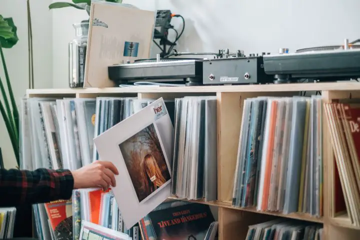 Young man holding a vinyl album cover in front of his collection.